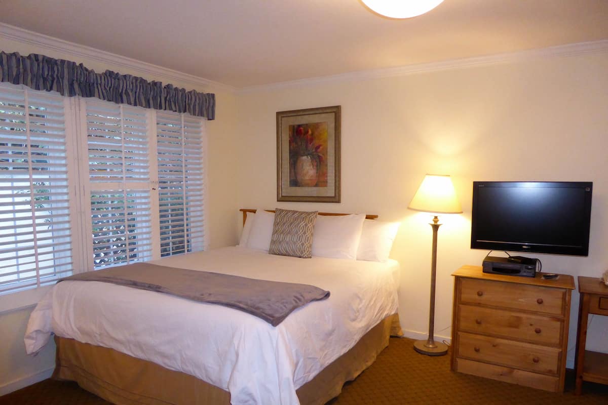 A hotel room with a bed, a television on a wooden stand, a lamp, and a painting on the wall.