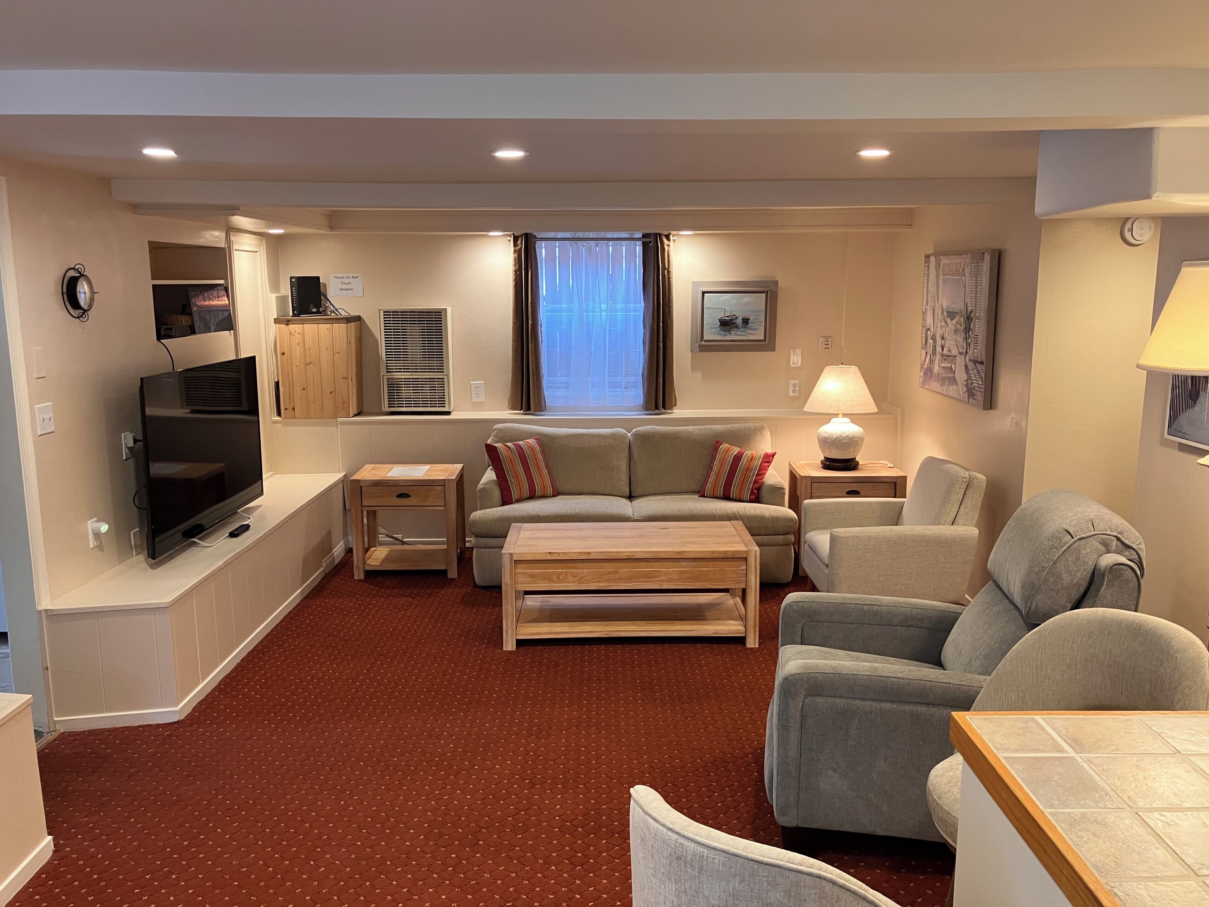 A living room with a sofa, armchairs, a TV, a lamp, and a window with curtains.