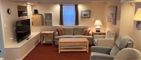 A living room with a sofa, armchairs, a TV, a lamp, and a window with curtains.