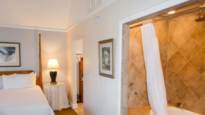 A hotel room with a bed, a bedside table with a lamp, a shower area with a bathtub, and a framed picture on the wall. - Briarwood Inn (Carmel)