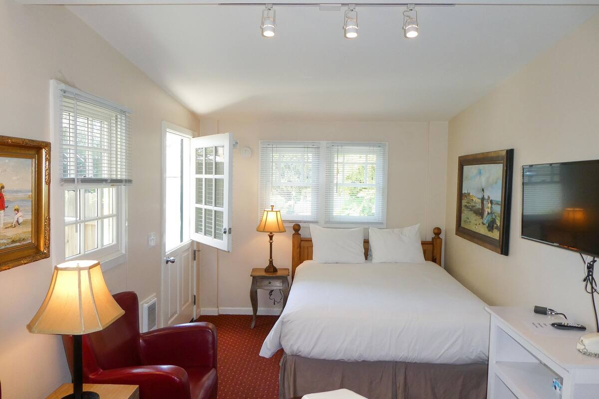A bedroom with a bed, a desk, a chair, a lamp, and a TV.