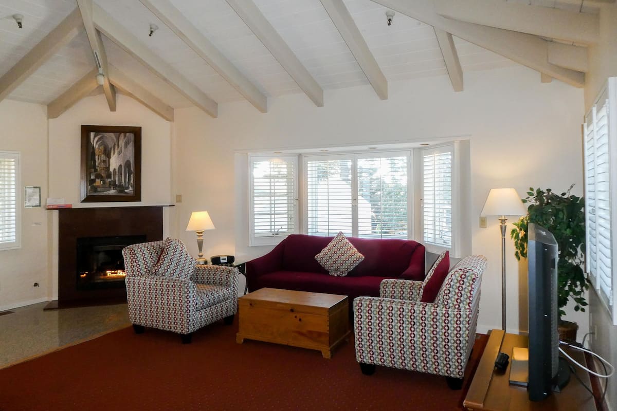 A living room with a fireplace, a red sofa, patterned armchairs, and a wooden coffee table.