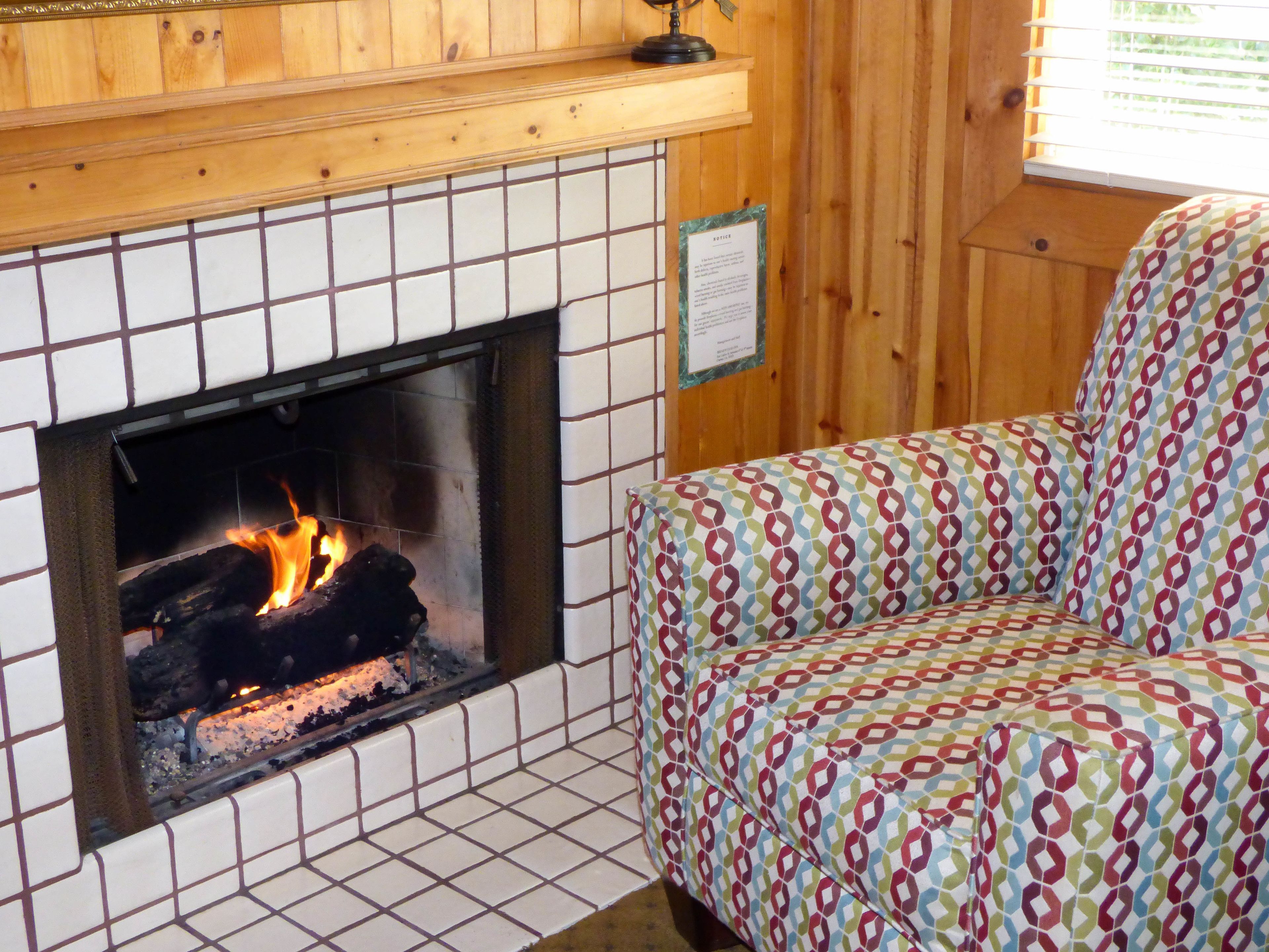Una habitación con chimenea de baldosas, un sofá estampado y paredes de madera.
