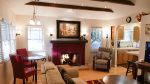 A living room with a fireplace, a sofa, a dining table, and a kitchen visible through an archway. - Briarwood Inn (Carmel)