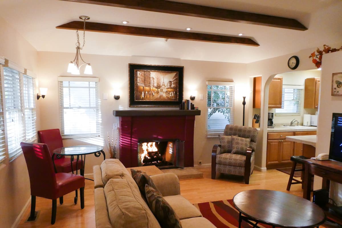 A living room with a fireplace, a sofa, a dining table, and a kitchen visible through an archway.