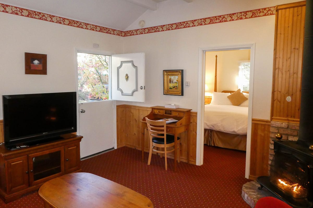 A cozy room with a television, a wooden desk, a chair, a bed, and a fireplace.
