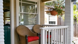 A porch with wicker chairs, a red cushion, and a white railing. - Briarwood Inn (Carmel)