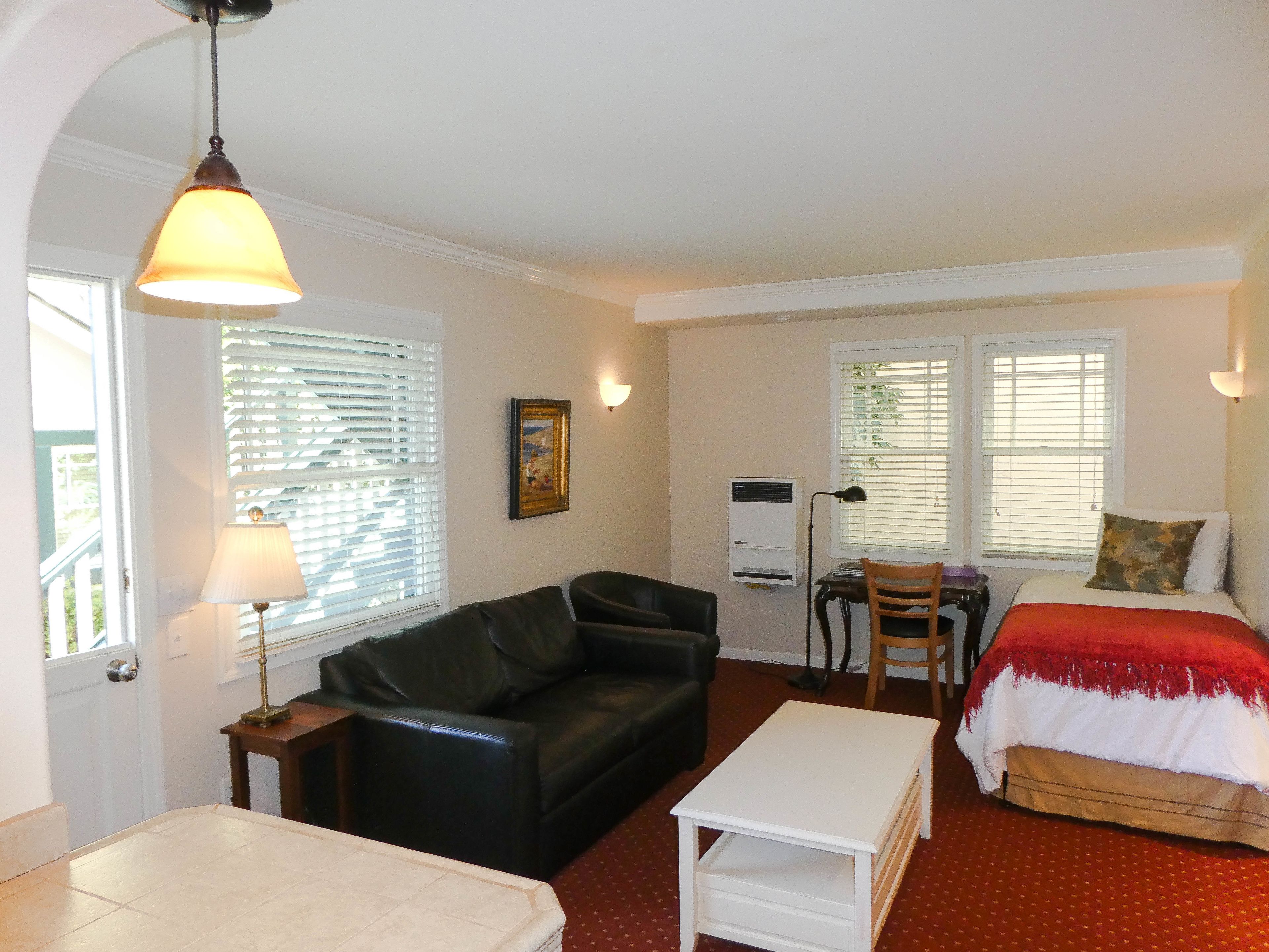 A compact room with a bed, a desk, a chair, a sofa, and a lamp.
