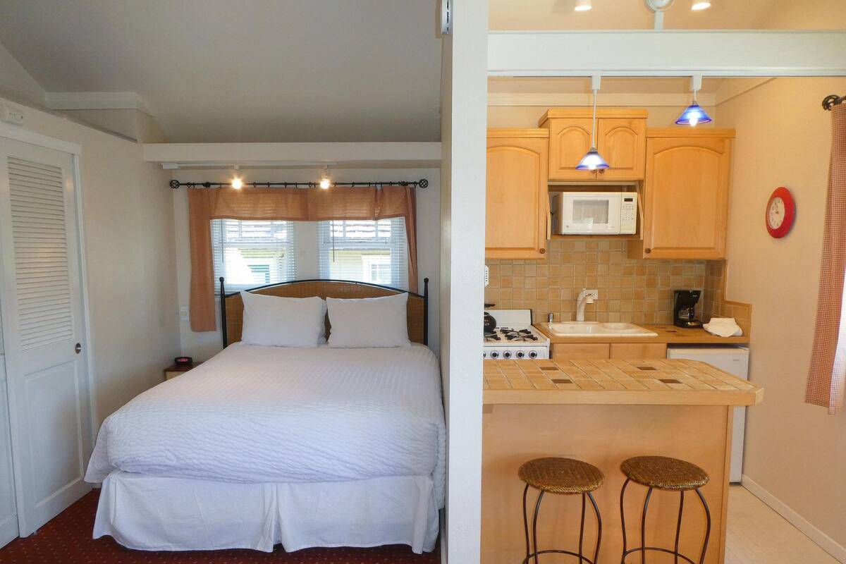 A compact room with a bed, a kitchenette, and a small bar area.