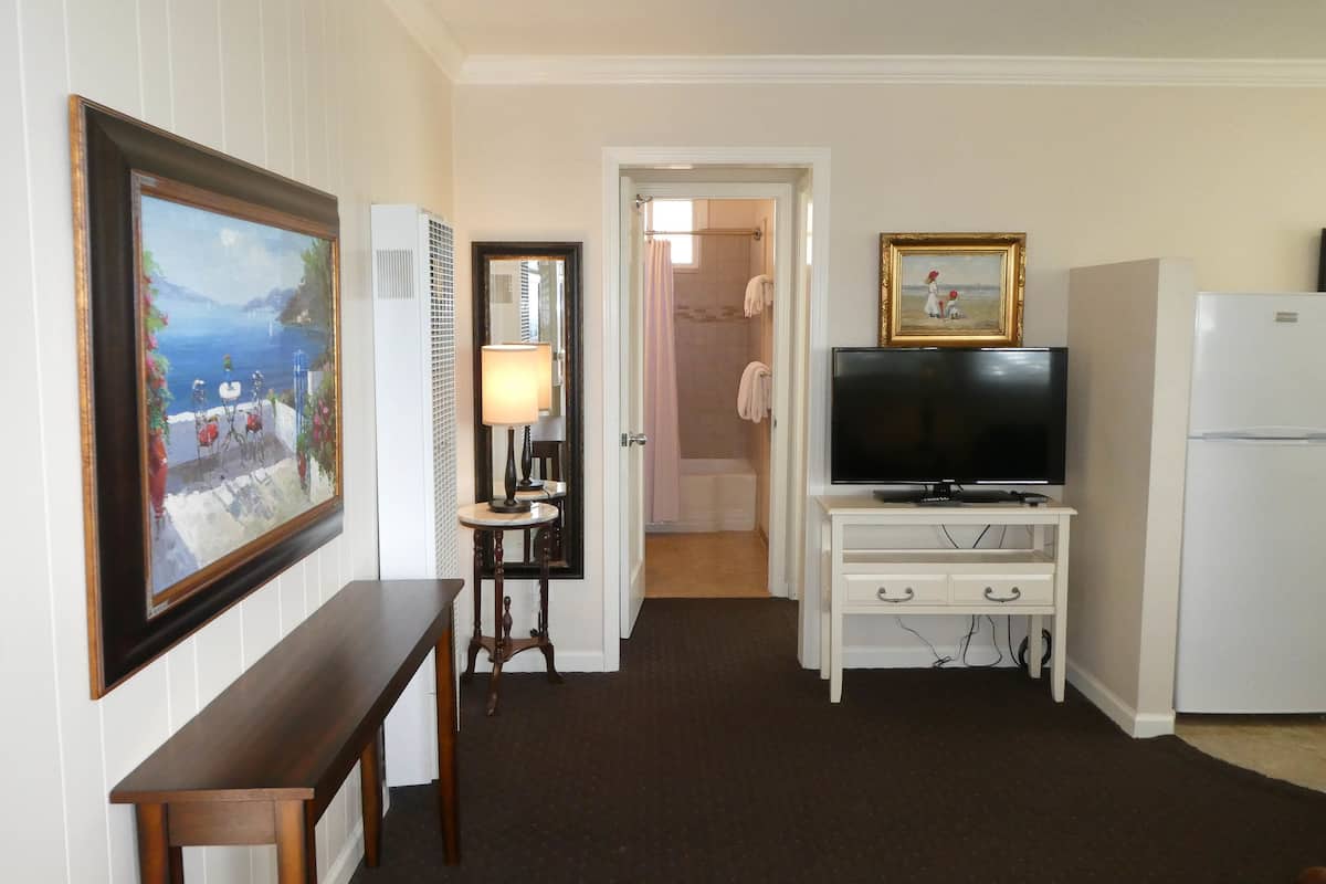 A hotel room with a television, a small table, a mirror, and a refrigerator.
