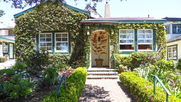A house with a brick pathway leading to a door with a flower arrangement, surrounded by lush greenery and a small garden. - Briarwood Inn (Carmel)