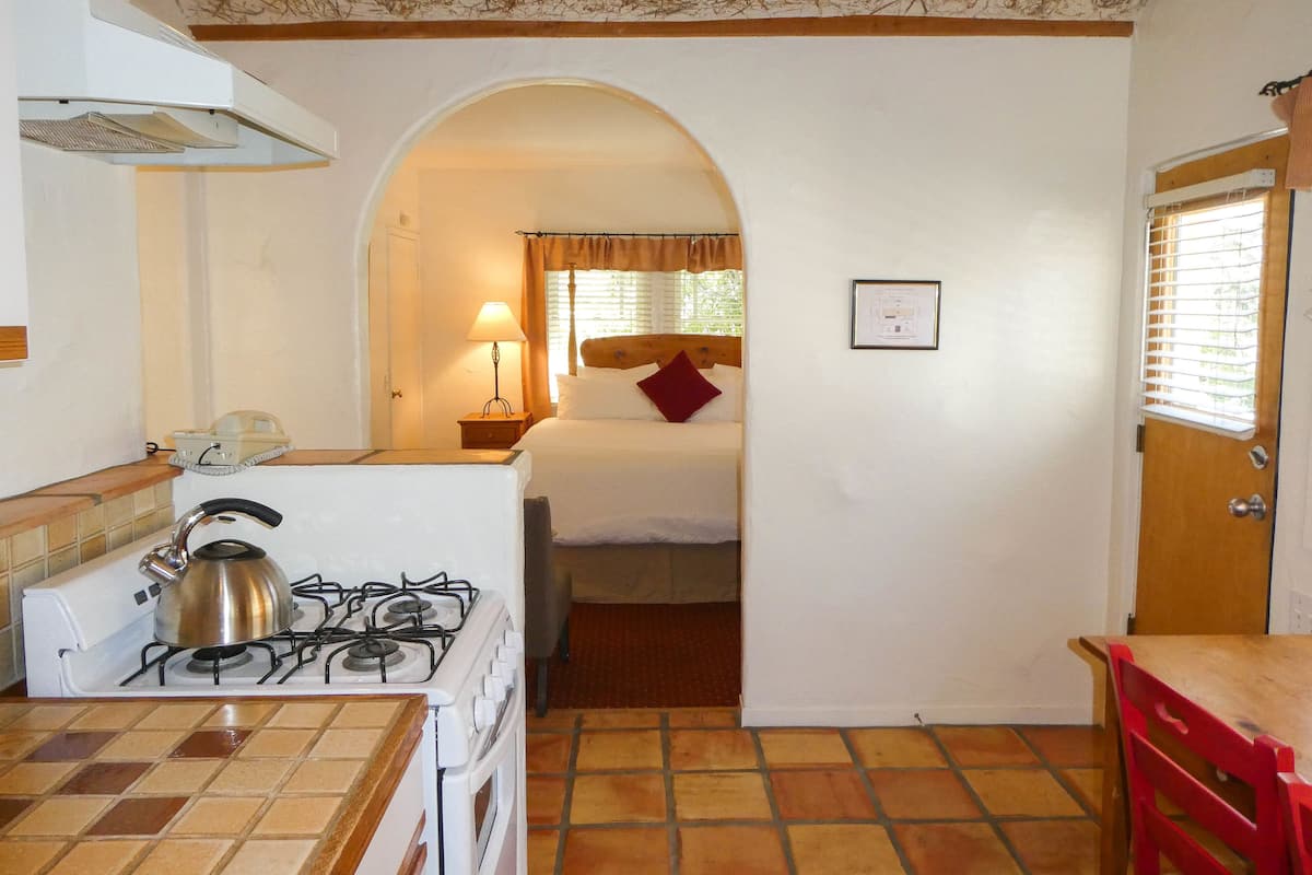A compact kitchen with a gas stove, a small table, and a red chair.