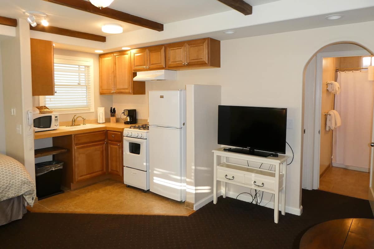 A compact kitchen with wooden cabinets, a microwave, a stove, a refrigerator, and a television on a white stand.