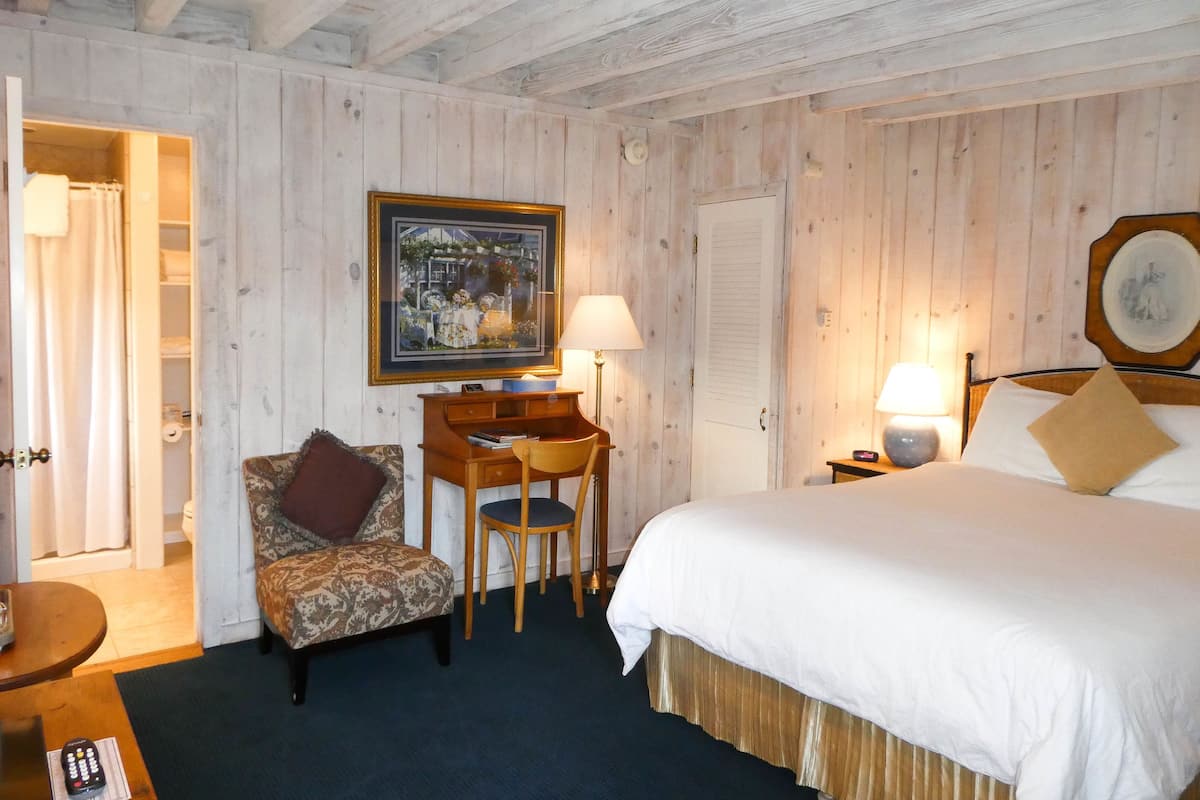 A hotel room with a bed, a desk, a chair, a lamp, and a painting on the wall.