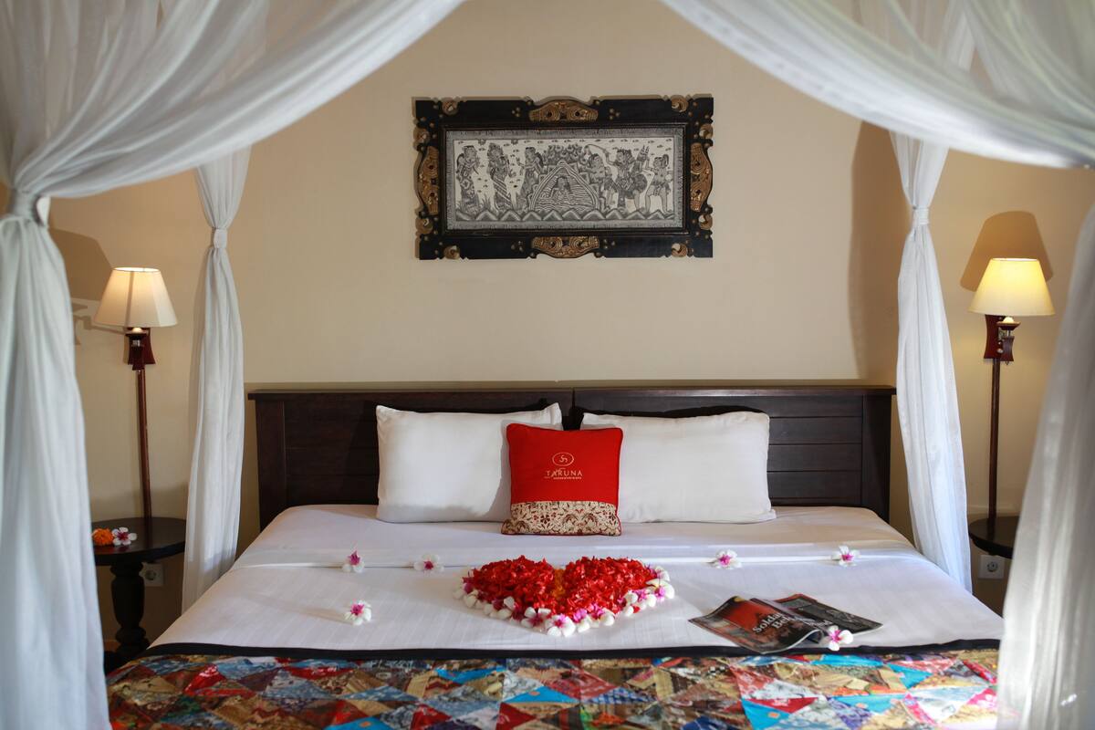 A neatly made bed with a red pillow, a decorative wall hanging, and a quilt with a geometric pattern.