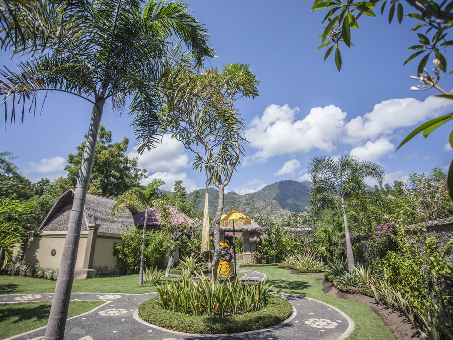 Un jardín tropical con una estructura de techo de paja, una estatua y un sendero pavimentado.