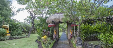 A pathway leading to a thatched-roof structure surrounded by lush greenery and tropical plants.