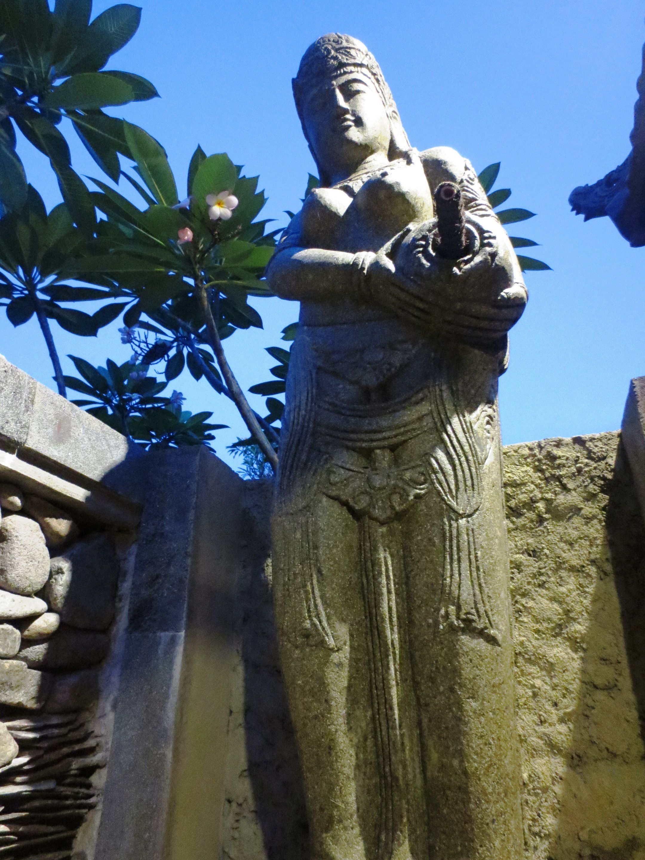Una estatua de piedra de una figura sosteniendo un cuenco, sobre un cielo azul despejado.