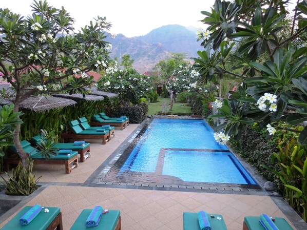 Un espace piscine doté de chaises longues et d’une piscine entourée de verdure, avec des montagnes en toile de fond.