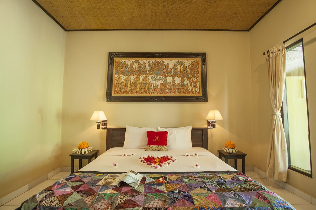 A hotel room with a large bed, two bedside lamps, a framed artwork above the bed, and a floral arrangement on the bed.