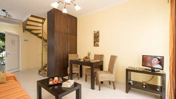 Un salon comprenant un canapé, une table à manger avec des chaises, un téléviseur posé sur un meuble, un escalier et une grande armoire en bois.