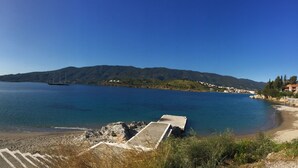 Vista costera con cielo despejado, un barco en el agua y un litoral rocoso con escalones que bajan a la playa.