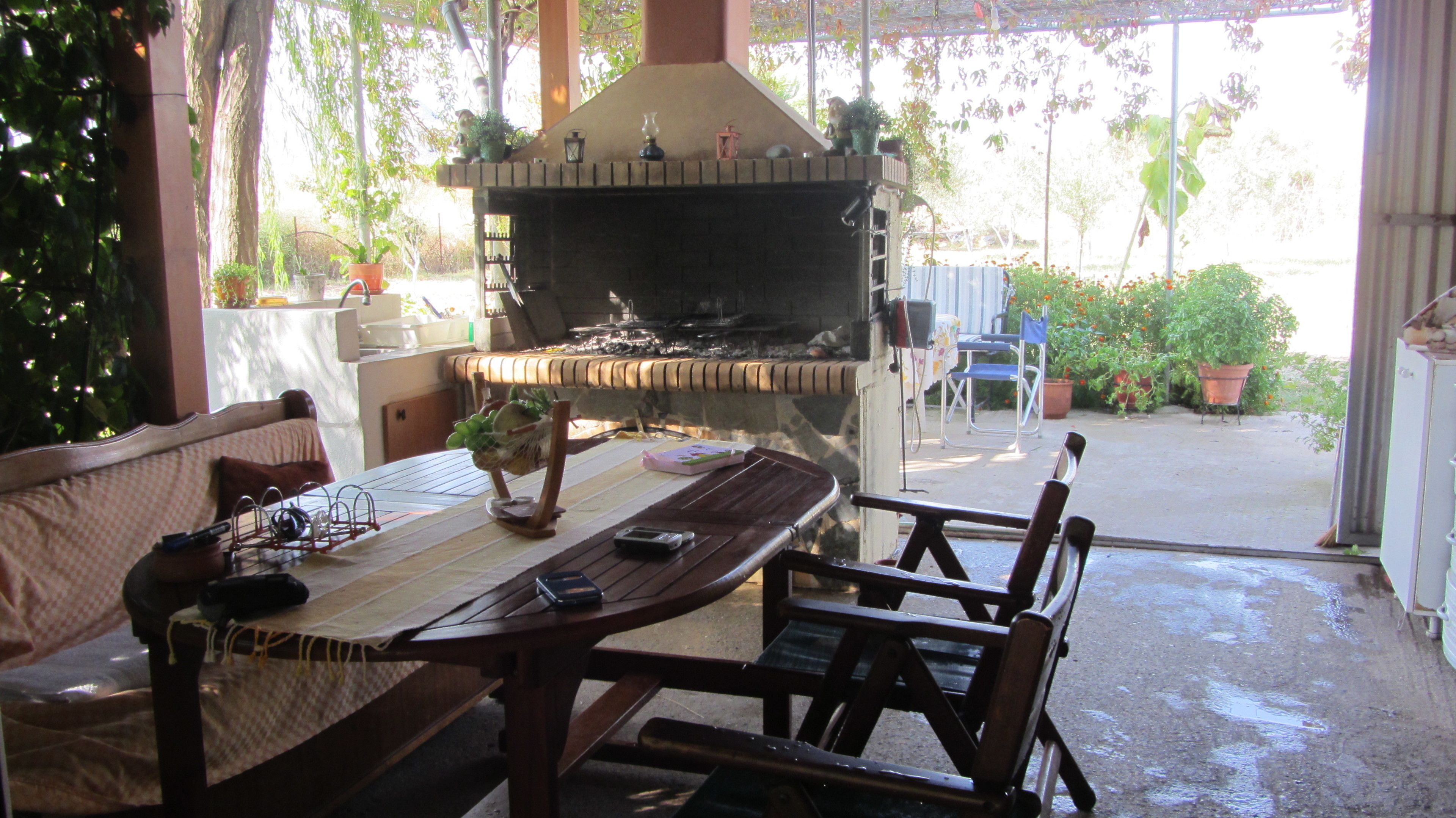 An outdoor patio with a wooden table and chairs, a barbecue grill, and potted plants.