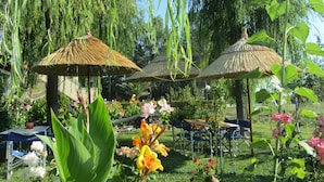 A garden with thatched umbrellas, outdoor seating, and lush greenery. - Shine Studios (Lesvos)