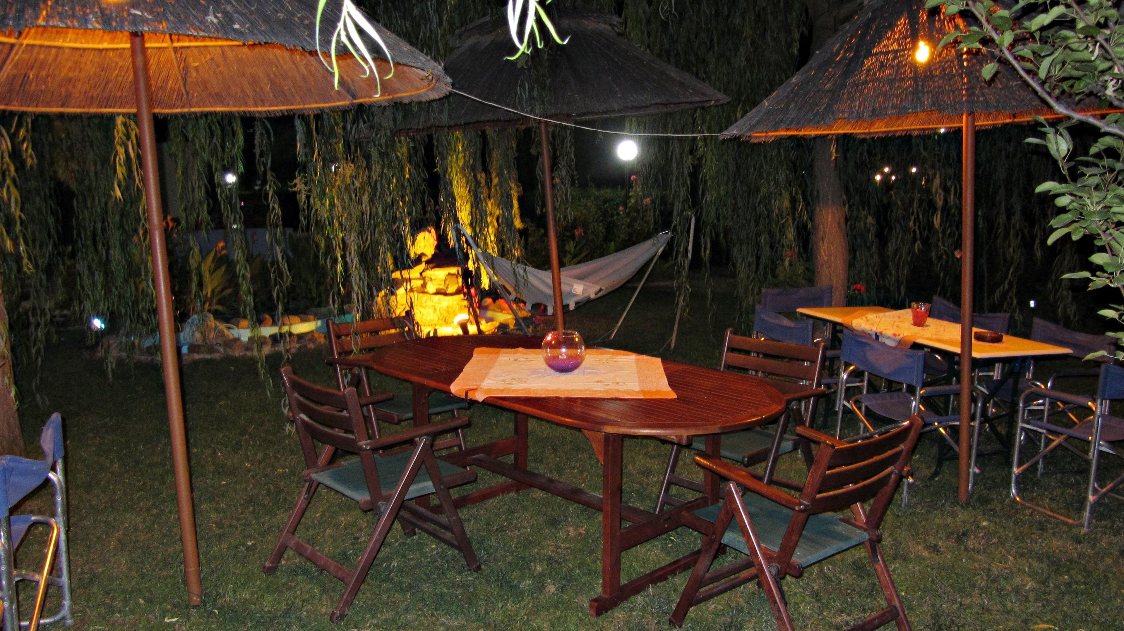 Een terras met houten tafels en stoelen, omgeven door rieten parasols, en een hangmat op de achtergrond.