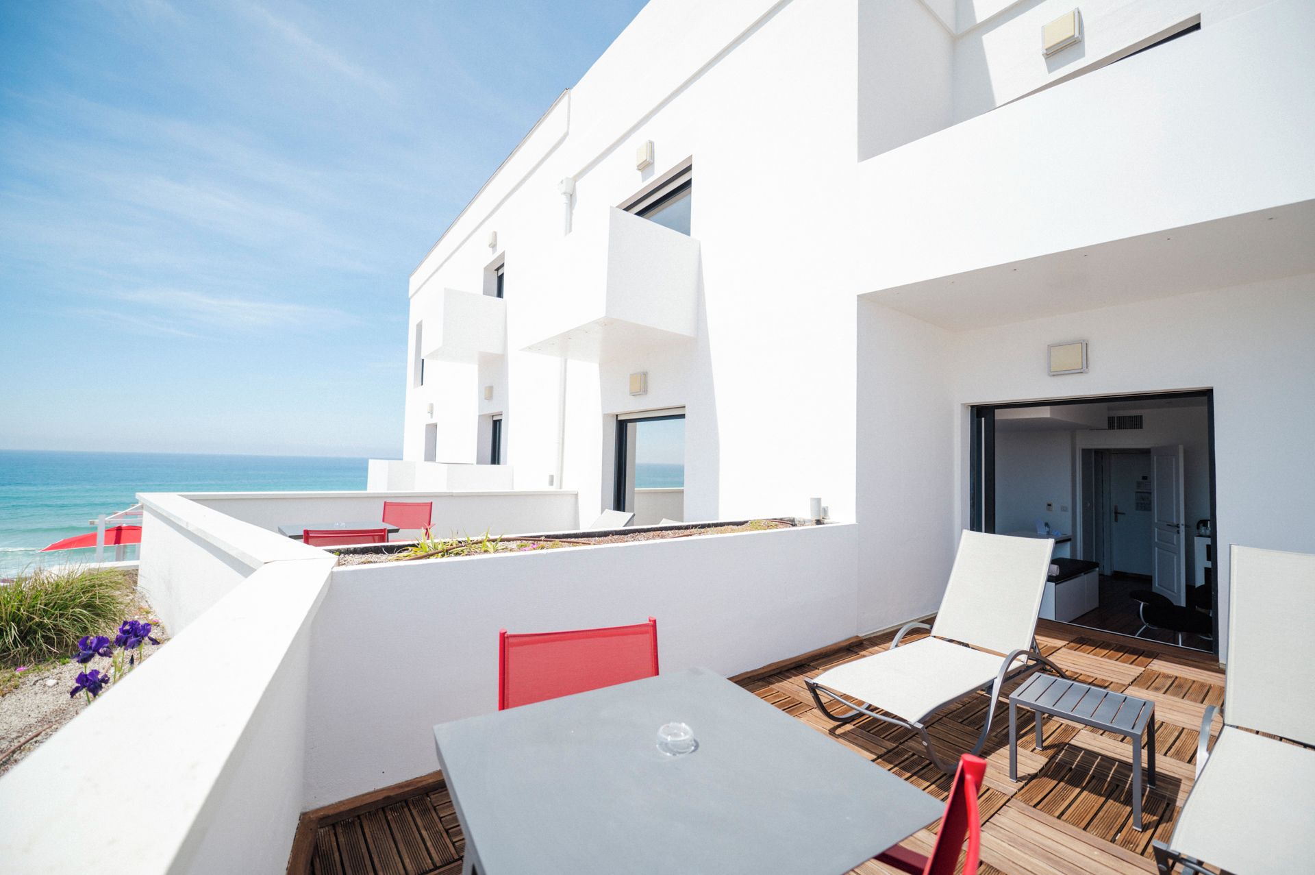 Eine moderne Außenpatio mit Blick auf das Meer, ausgestattet mit einem Tisch und Stühlen, sowie einem roten Sessel.