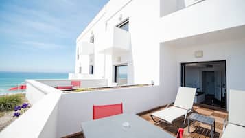 A modern outdoor patio with a view of the sea, featuring a table and chairs, and a red chair.