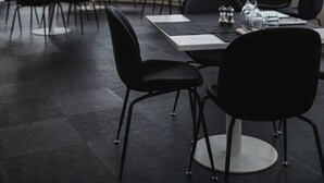 L’intérieur d’un restaurant moderne, avec de grandes fenêtres, des chaises noires et des tables dressées pour le service.
