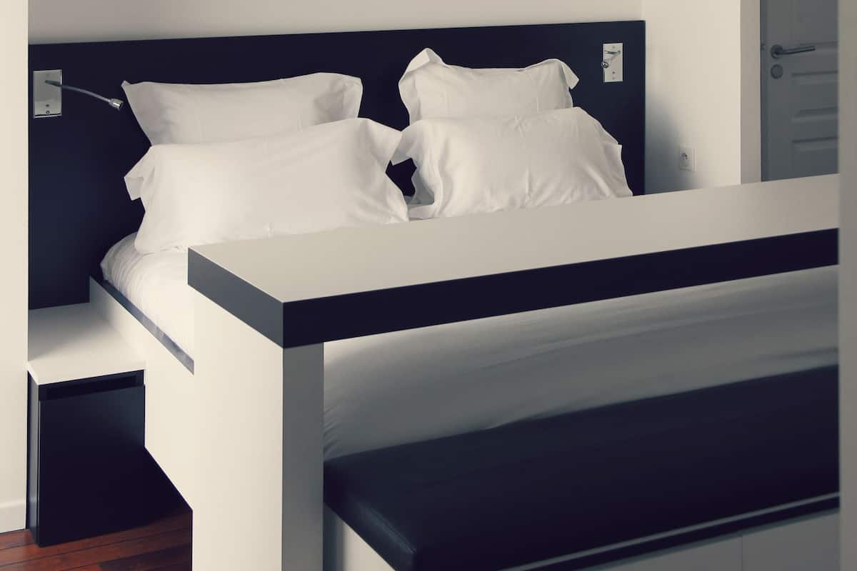 Une chambre à coucher moderne avec un lit, du linge de lit blanc et une tête de lit sombre.