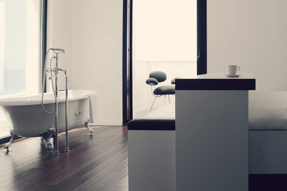 Une chambre moderne avec un grand lit, une table de chevet, une commode, une fenêtre et une salle de bain équipée d’une baignoire et d’une douche.