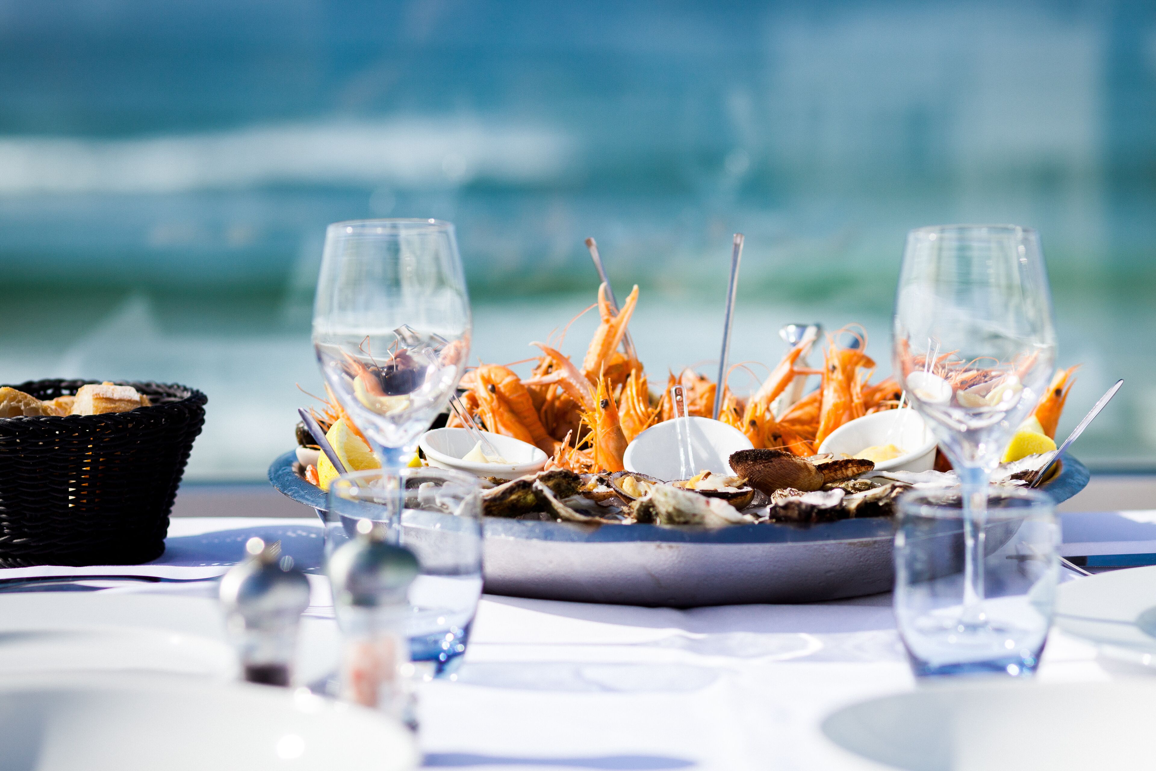 A seafood platter with wine glasses on a table by the sea.
