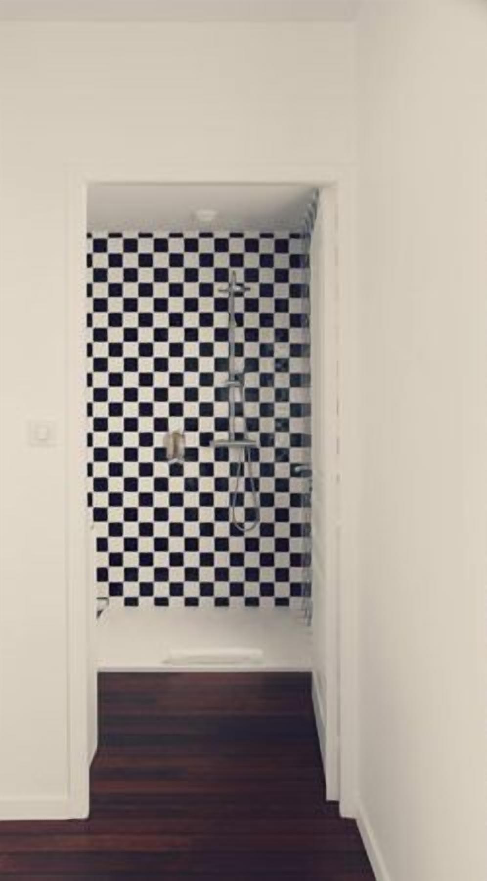 A narrow hallway with a checkered tile wall and a dark wooden floor.