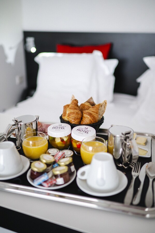 Un plateau de petit-déjeuner avec des croissants, du jus et des confitures, posé sur le lit d’un hôtel.