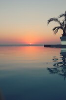 A serene sunset over a calm body of water with a palm tree and a modern structure reflecting on the surface.