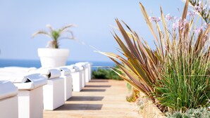 Une terrasse en bois avec des chaises longues blanches et une plante en pot.