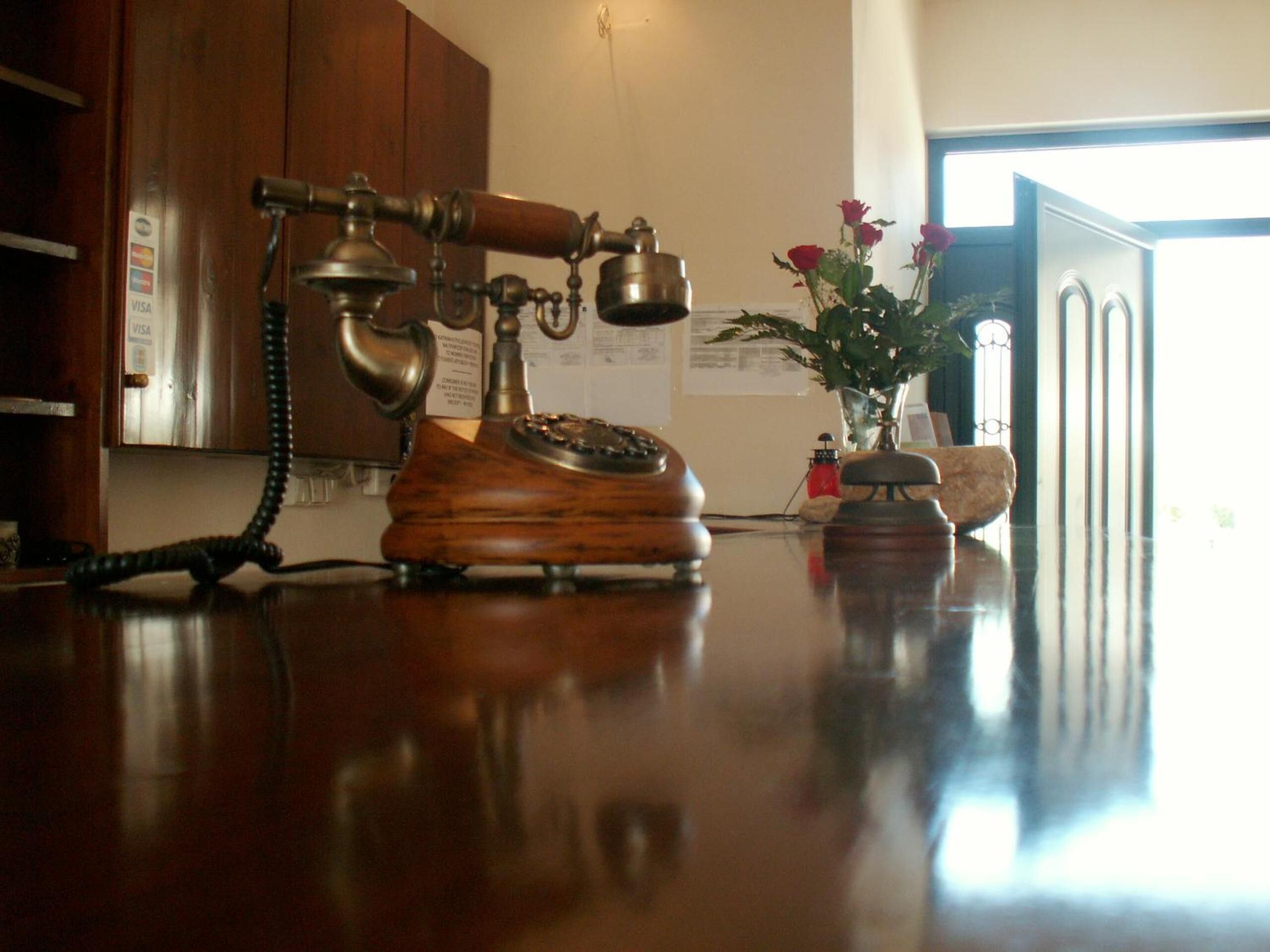 Un vieux téléphone à cadran rotatif, posé sur un bureau en bois, avec un vase de fleurs et une petite bouteille.
