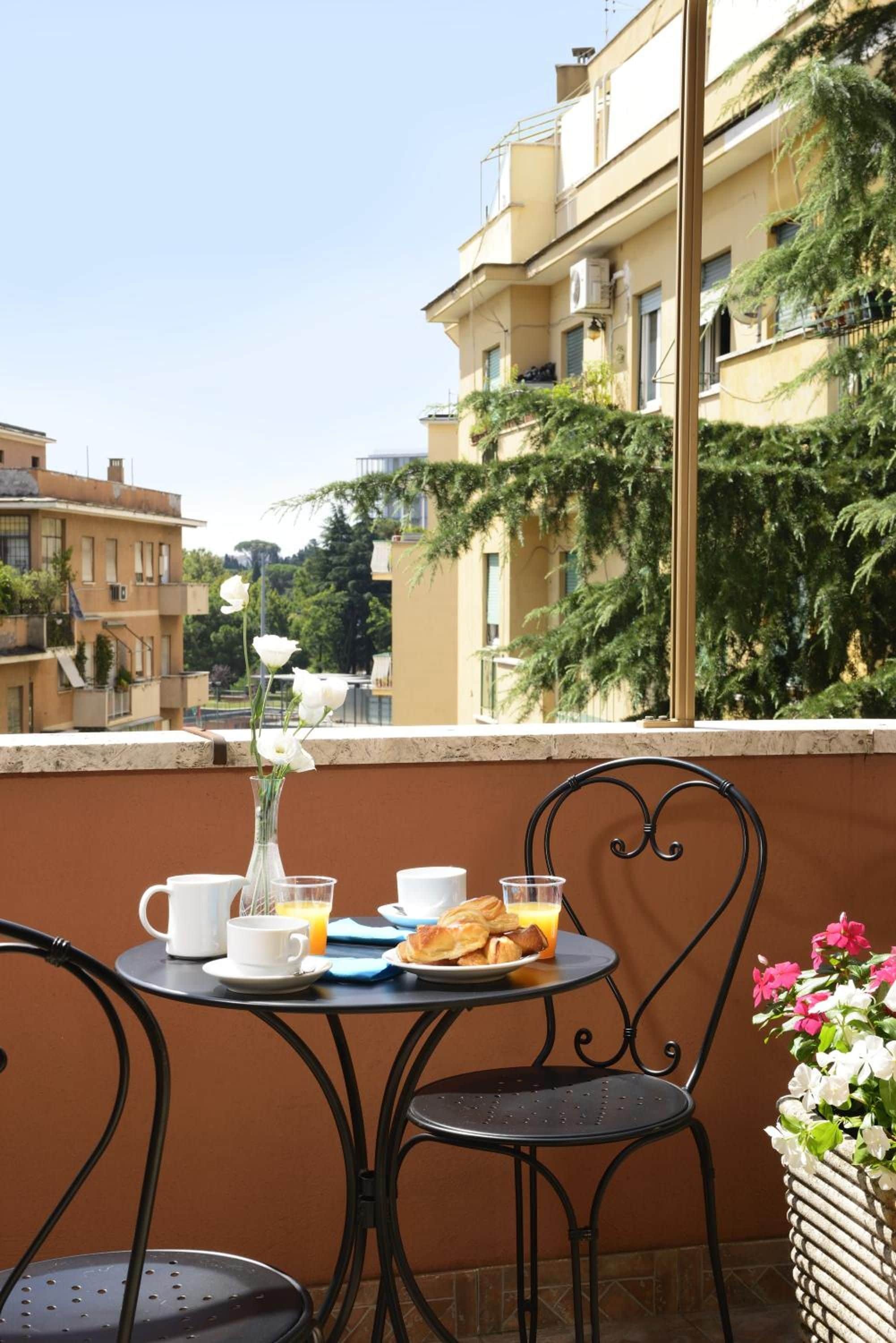 A balcony with a table set for breakfast, including a vase with flowers, a plate of pastries, and a glass of orange juice.
