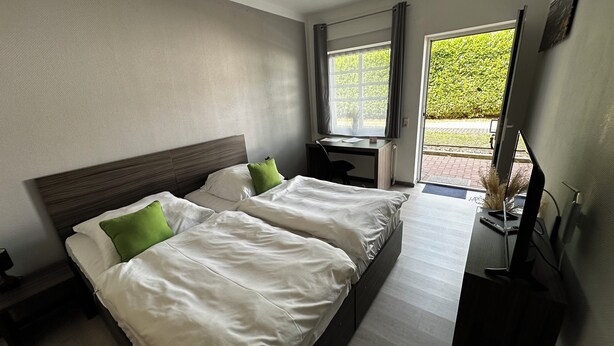 A hotel room with two beds, a desk, and a window with a view of greenery. - Messe Motel Laatzen (Laatzen)