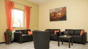 A living room with two black sofas, a coffee table, and a large window with orange curtains. - Messe Motel Laatzen (Laatzen)