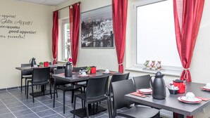 A dining area with tables and chairs, red curtains, a black and white cityscape picture on the wall, and a window with red curtains. - Messe Motel Laatzen (Laatzen)