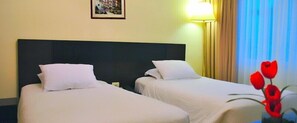 Een hotelkamer met twee enkele bedden, een nachtkastje, een lamp en een schilderij aan de muur.