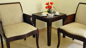 Deux chaises en bois avec des coussins beige, une petite table sur laquelle est posé un vase de fleurs rouges, un journal et deux tasses.