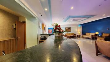 A hotel lobby with a reception desk, seating area, and a large vase of flowers.