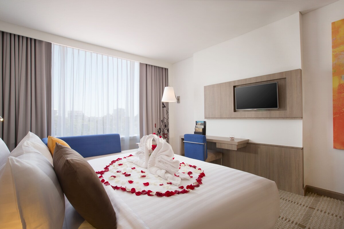 A hotel room with a bed, a desk, a TV, and a large window with curtains.