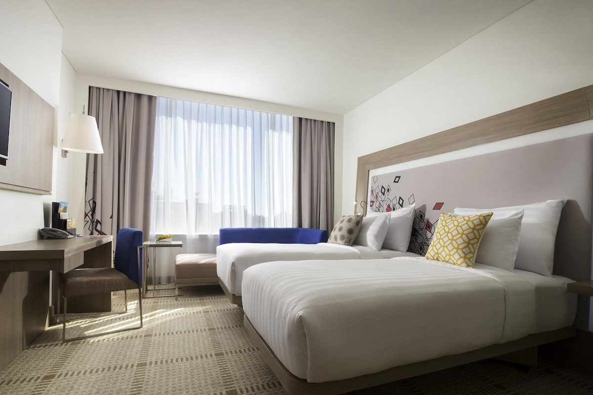 A hotel room with a large bed, a desk, a chair, and a small table.
