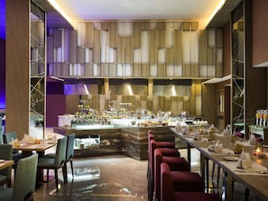 A modern restaurant with a central bar, seating on both sides, and a high ceiling with a geometric design.